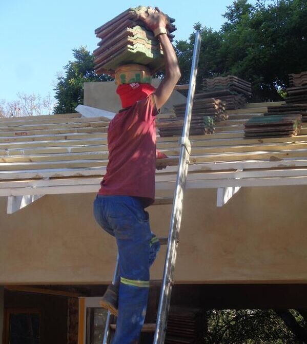 A man carrying shingles on to the top of a roof 