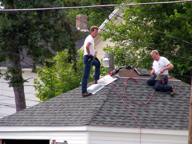 Roofing contractors with heavy tools on a roof