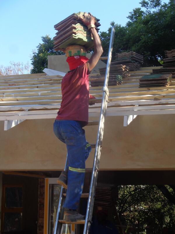 A person carrying shingles onto the top of a roof